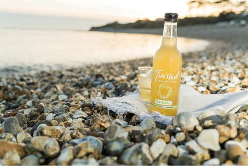 Bottle of Twisted Lemonade on a pebbly beach with a scenic background